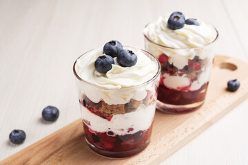 Trifle - traditional English dessert. Two portion in glasses on a light wooden table.