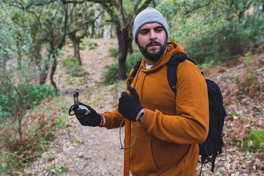 Chico con barbar muy alto con brujula en un bosque y equipamiento de senderismo