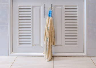 Closeup of the fabric hand towel is hanging near the white door of the cabinet.