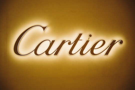 Dubai, UAE, United Arab Emirates - May 28, 2021: Close golden logotype Cartier (jeweler) Brand at wall of store in shopping center. Cartier International SNC, Cartier is French luxury goods