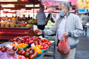 Middle aged man in mask buying tomatoes