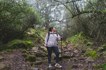 Naklejka na ściany i meble Chica joven guapa en mitad de sendero de un bosque con niebla realizando senderismo
