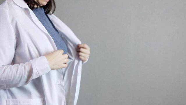 unrecognizable female doctor putting on white uniform lab coat, preparing visit patient. brunette female physician wearing medicine clothes, put on medical gown. nurse practitioner dressing up