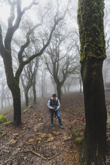 Fototapeta premium Chico con equipo de senderismo haciendo una foto en medio del camino de un bosque lleno de niebla