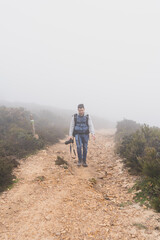 Chico joven bajito andando por camino de piedra rodeado de niebla y tomando fotos