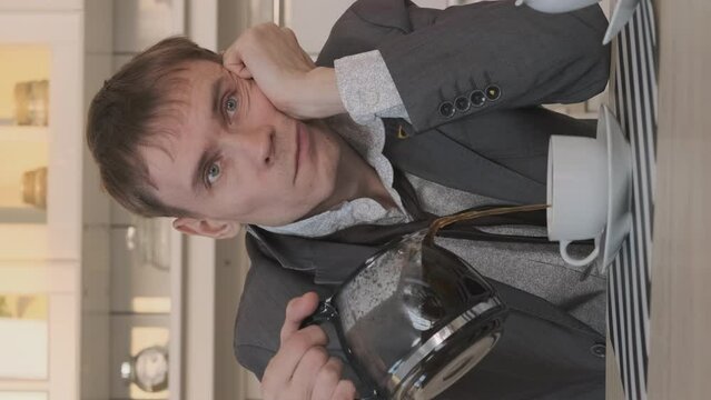 Vertical Video. Tired Man Pouring Coffee Early in the Morning, Having Breakfast after Sleepless Night. Coffee Spills over the Rim of Cup