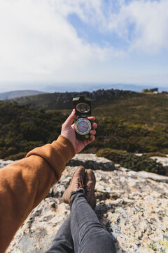 Vista en primera persona de paisaje de monta&ntilde;a con una mano sujetando una br&uacute;jula y los pies de una persona tumbada