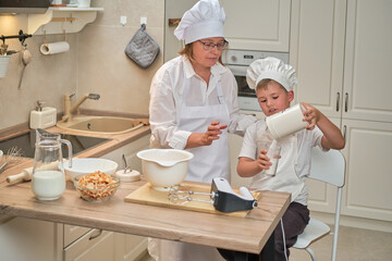 Mother and son cooking apple pie in the home kitchen. A woman and a boy in chef hats and aprons cook with pastries