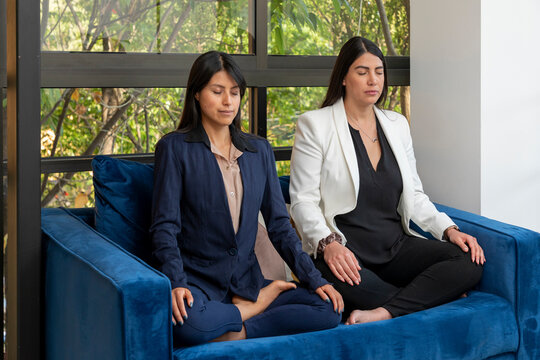 Side view of two businesswomen meditating on an armchair while taking a break at work in the office