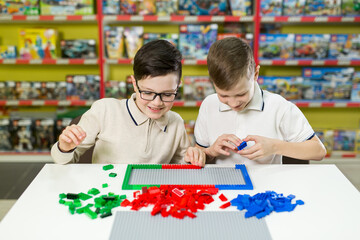 Fototapeta premium Children play in the designer at the table. Two boys play together with colored plastic blocks in the gaming center, school.
