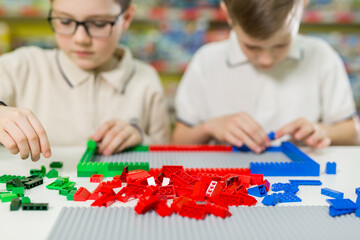Fototapeta premium Children play in the designer at the table. Two boys play together with colored plastic blocks in the gaming center, school.