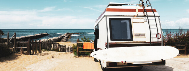 Horizontal banner or header with rear view of vintage camper parked on the beach against a scenic...