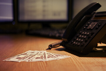 Landline phone and cash dollars on the table, close-up. Office desk in a dark night room with...