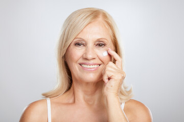 An attractive blond senior woman putting anti-age creme. Beauty photography