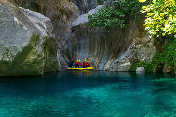 tourists and guide on an inflatable boat float down a rocky canyon with blue water in Goynuk, Turkey