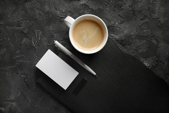 Photo of blank business card, coffee cup, pen, usb flash drive and slate plate on black stone background.