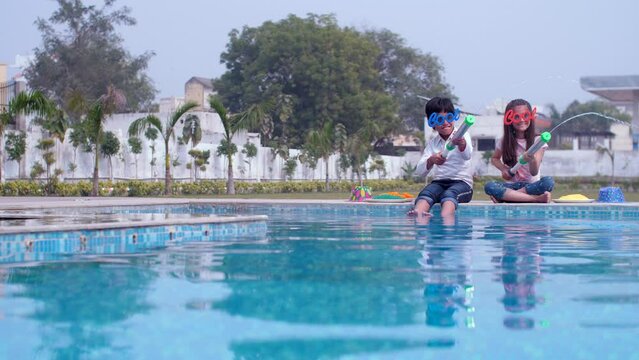 School kids wearing funny goggles playing with a water gun (Pichkari) on Holi - stylish  an Indian festival  a happy childhood. Adorable friends / siblings in casual clothes relaxing by the poolsid...