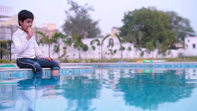 A smiling young boy enjoys eating yummy ice cream during the Holi festival celebrations - leisure time  an Indian festival  a tasty cuisine. A little kid in casual clothes enjoys eating an ice-crea...