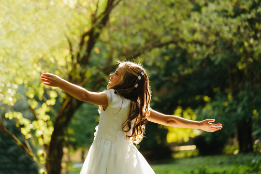 Happy girl dancing in park in First Communion dress