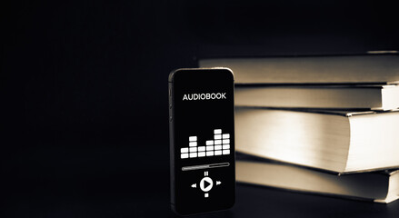 Audio listen book. Phone screen with audiobook app on paper books black background. Online education course, E learning class and e book digital technology concept.