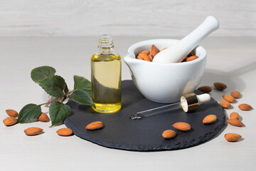 Almond oil in a bottle, pipette, bowl with almond kernels on a black board on a light background,...