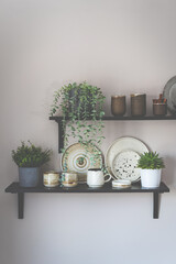 Stylish open space shelves with authentic handmade ceramic dishes, plants and plates. Design interior of cozy kitchen