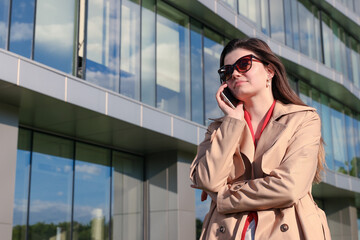 A young woman in business clothes talks on the phone in the background of an office building