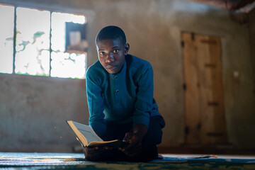 African teenage boy sitting and reading book in poor school, high quality photo