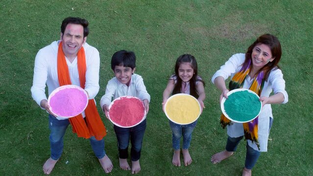An attractive couple and their children wish everyone on Holi with a plate of Gulal - togetherness and bonding  happy faces  an Indian festival. A modern Indian cheerful family celebrating the Indi...