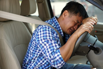 Asian man is sad and crying in car. His face down on the steering wheel. Concept :  Concept :...