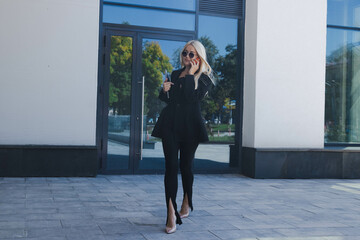 Obraz premium A young woman in a suit is talking on the phone and holding a laptop in her hands on the street