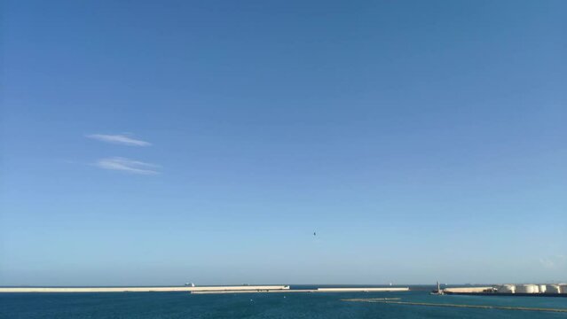 Time lapse of the horizon by a port. Most of the view is covered by a clear blue sky where many seagulls fly by quickly, gliding across the sky.