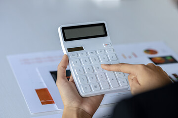 Businessman using a calculator to calculate numbers on a company's financial documents, he is analyzing historical financial data to plan how to grow the company. Financial concept.