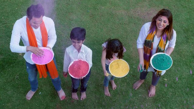 A young couple and their little kids throwing colors in the air while playing Holi - organic Gulal  a safe Holi  enjoyment. A modern Indian family dressed in ethnic attire for celebrating the India...