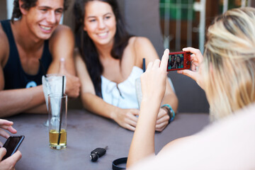 Capturing their happiest memories. Group of teens enjoying beverages while at an outdoor restaurant while taking a photo with a mobile phone.
