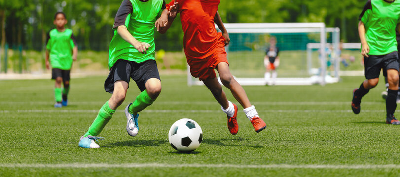 Horizontal image of teenagers playing football. Happy boys kicking classic soccer ball on grass field. School children compete in sports game on training pitch