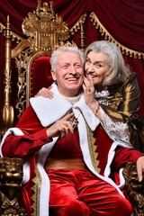 Portrait of senior man in red cloak sitting in vintage chair