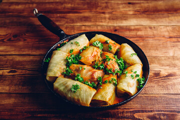 Cabbage Rolls Stuffed with Minced Meat in Frying Pan Served with Chopped Parsley on Wooden Table