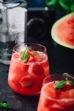Glasses of watermelon and strawberry cocktail with mint garnish on dark concrete background