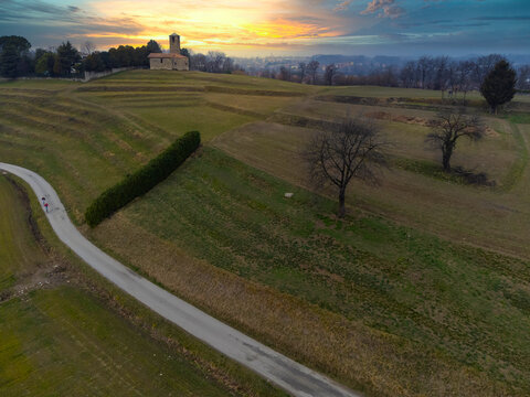 Aerial view of two people, cycling along road with Rural church in the distance, Garbagnate Milanese, Lombardy, Italy