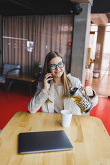 A modern woman of Slavic appearance, a manager in a light jacket and glasses, a girl with a smile on her face, sits at a table in a cafe and drinks tea. Remote work