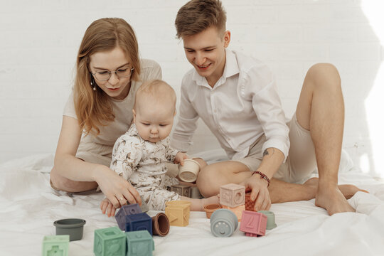 Portrait Of Young Happy Family Sitting With Little Cute Plump Infant Baby Playing With Modern Pastel Silicone Bowls.