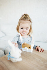 Small adorable girl playing with wooden toy camera and fluffy rabbit toy