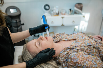 An esthtetician microneedling a spa client as she lies on a table in a health and wellness medical...
