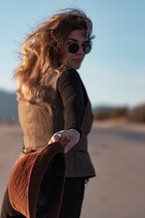 Close up photo of young woman with sun glasses. She pass her hat towards to camera. The focus is on...