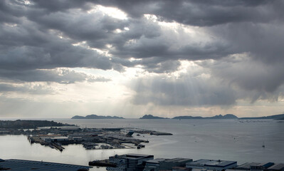 Vista general del puerto de Vigo y su ría con las Islas Cíes de fondo y cielo con nubes en claroscuro y tonos fríos al atardecer