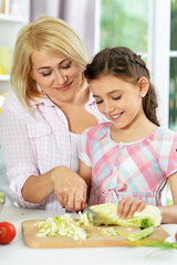 Cute little girl with her mother cooking together at kitchen table