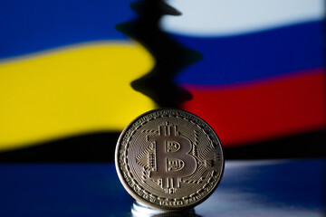 Metal coin Bitcoin on the background of the Ukrainian and Russian flag. The concept of economic sanctions