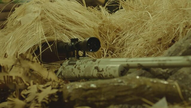 Close up view of sniper dressed in ghillie suit or grass cloak waiting and looking by rifle optics . Sharpshooter aims and shoots . Sharp shooter shooting . Shot on ARRI movie camera in Slow Motion

