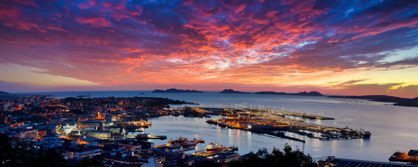 Vista general de Vigo al atardecer con la ciudad y el puerto en primer término y las Islas Cíes de fondo con un increíble cielo de nubes en tonos anaranjados - obrazy, fototapety, plakaty